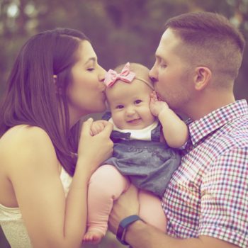 an adoptive couple kissing their baby girl.